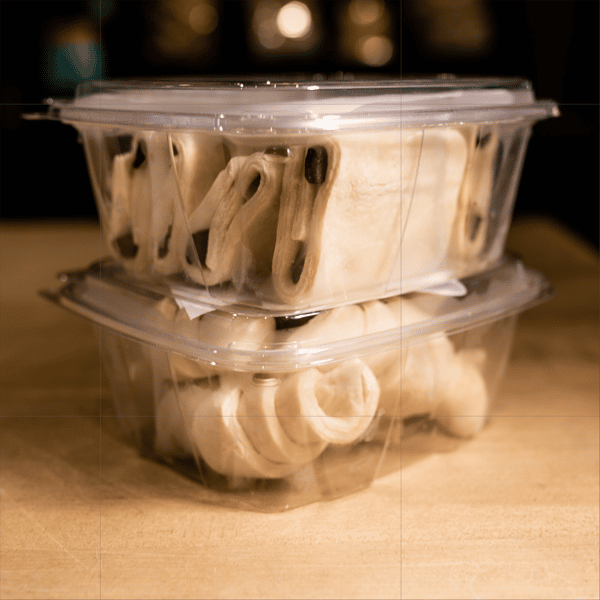 Two clear plastic containers stacked on top of each other, filled with uncooked bagels or similar baked dough items.
