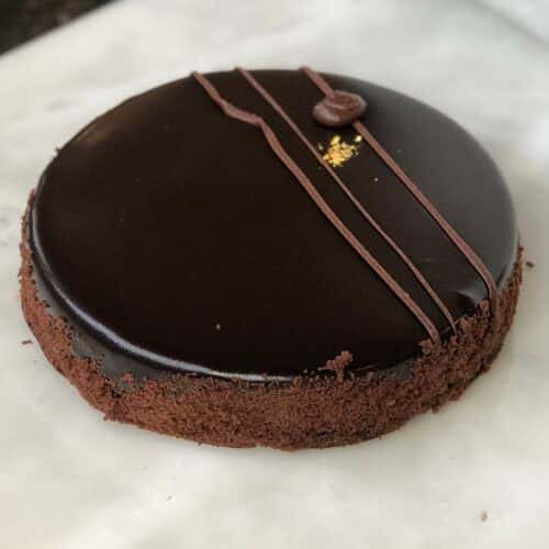 A chocolate cake with a glossy ganache topping, decorated with chocolate drizzle and a coffee bean on top.