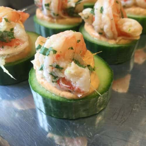 Cucumber slices topped with shrimp and garnished with fresh herbs, served as bite-sized appetizers.