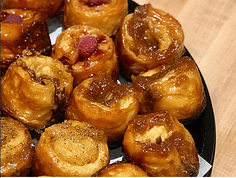 A plate of sweet pastry rolls, filled with various toppings like raspberry, caramel, and nuts, arranged in a circular pattern.