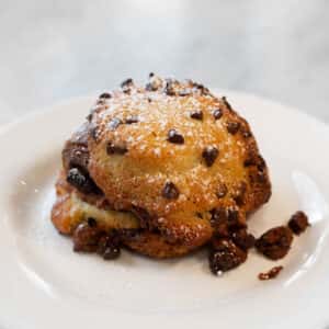 A freshly baked pastry with chocolate chips, lightly dusted with powdered sugar, served on a white plate.