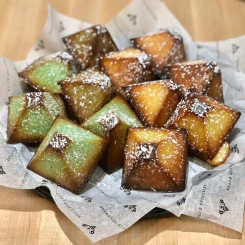 A tray of square, powdered sugar-dusted cakes with a golden-brown exterior and soft, slightly greenish interior.