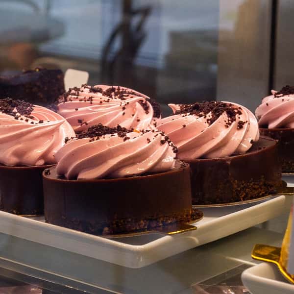 A display of individual chocolate desserts with a pink swirled frosting, topped with crumbled chocolate, arranged on a white plate.