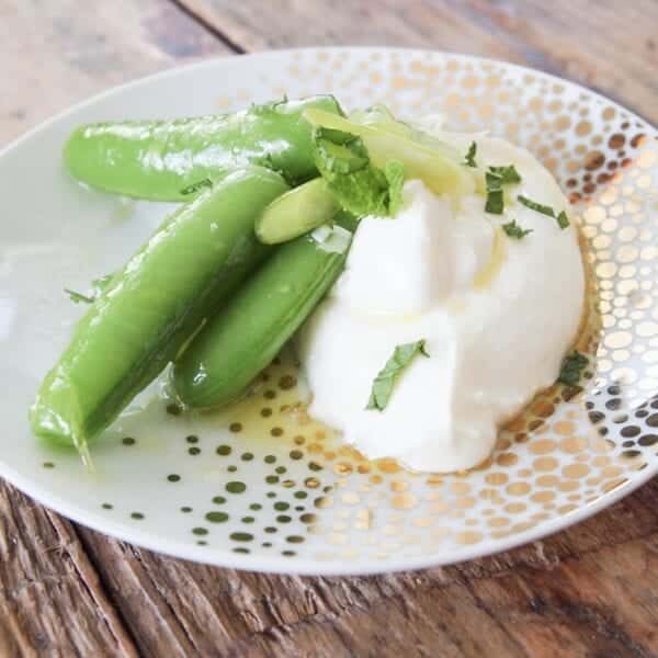 A plate of steamed green beans and fresh yogurt, garnished with chopped mint and a drizzle of oil.
