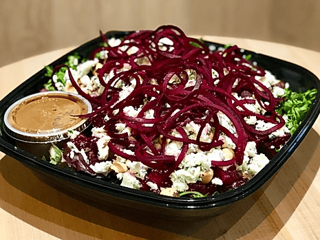 A salad with fresh greens, topped with beetroot spirals, crumbled cheese, and nuts, accompanied by a side of dressing.