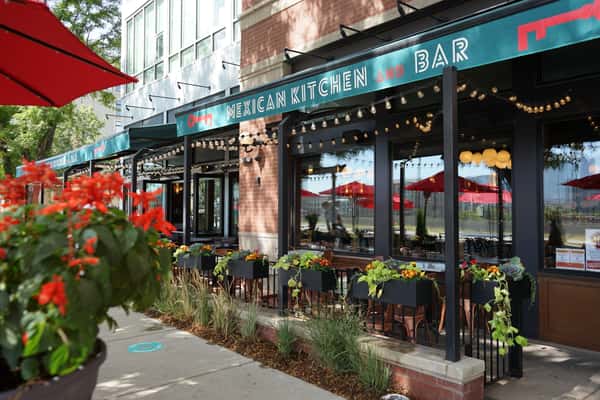 Outdoor patio seating at a neighborhood Mexican kitchen and bar with string lights, colorful planters, and inviting dining atmosphere.