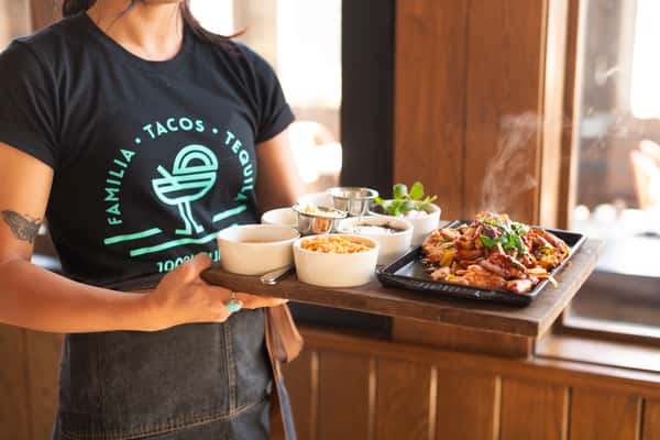Restaurant server presenting a sizzling fajita platter with house-made sides, showcasing fresh Mexican-inspired cuisine and warm hospitality.