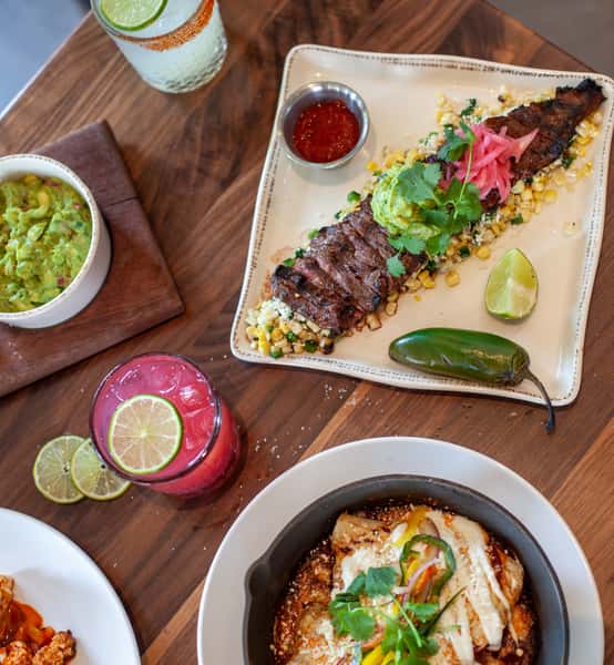 Grilled skirt steak served over roasted corn with guacamole, pickled onions, and fresh lime, paired with handcrafted cocktails.