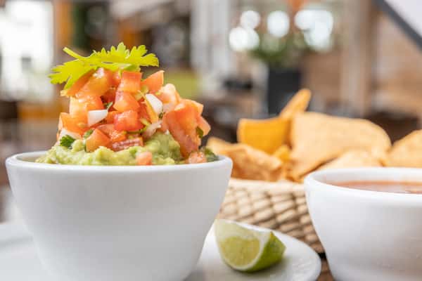 Guacamole topped with pico de gallo and cilantro, served with tortilla chips, salsa, and a lime wedge.