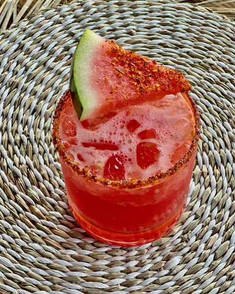 Spicy watermelon cocktail garnished with a chili-rimmed glass and a slice of watermelon coated in chili powder.