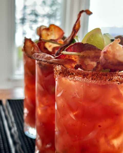 Spicy Bloody Mary cocktails garnished with crispy bacon, lime wedges, and a chili-rimmed glass.
