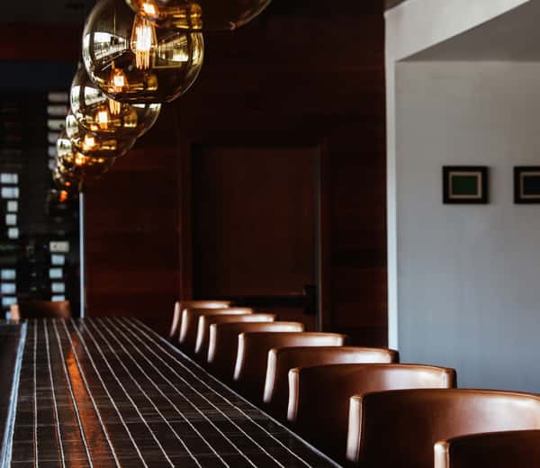 Inside Kayne Prime, an American Steakhouse, with brown leather chairs, a striped wooden table, and modern golden light fixtures creating a sophisticated dining ambiance.