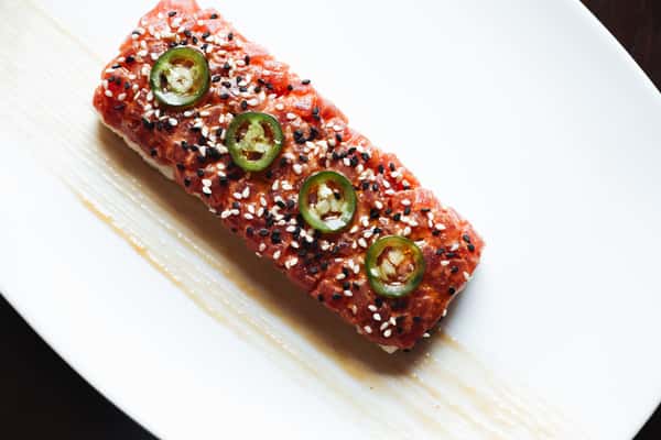 Delight in a seafood masterpiece on a white plate, topped with sesame seeds and jalapeno, showcasing the artistry of culinary craftsmanship.