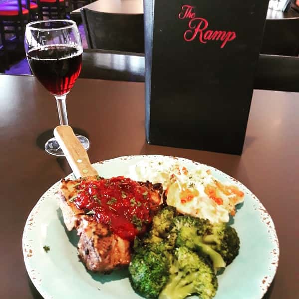 A chicken dish with tomato sauce drizzled on top, broccoli, and a glass of wine on the side