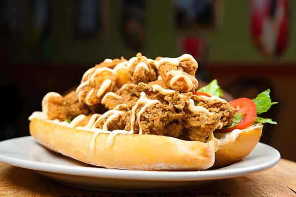 A fried chicken po' boy or sub sandwich, featuring crispy breaded chicken pieces drizzled with a creamy white sauce on a long roll.