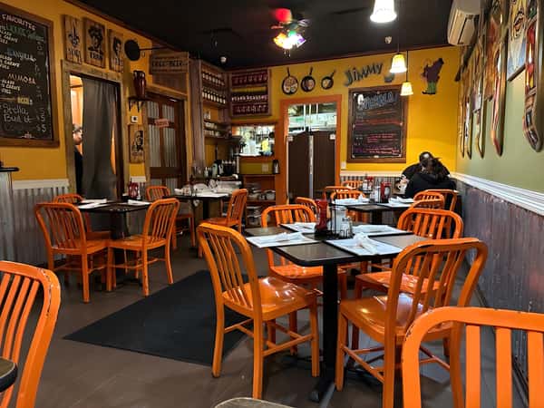 An interior shot of a restaurant dining area featuring orange wooden chairs, dark tables, and warm lighting.