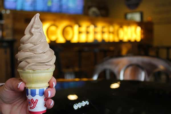 an ice cream cone with chocolate soft serve with the illumincated coffeehouse sign in the background