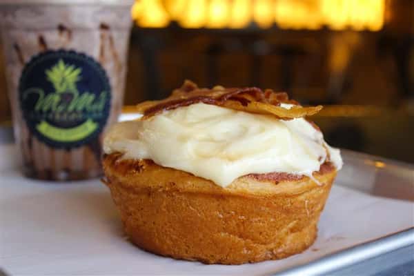 a cinnamon bun with bacon on top with a coffee drink in the background