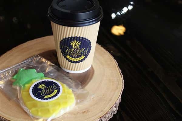 a coffee drink with a pineapple shaped and colored cookie next to it