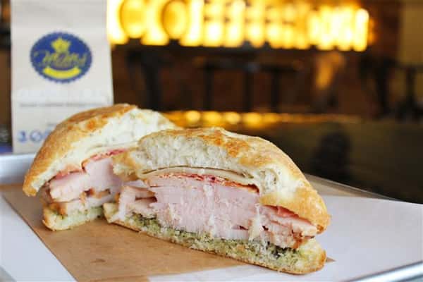a turkey sandwich cut in half with a bag with the mimi's logo in the background