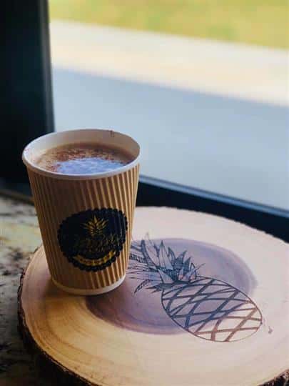 a coffee drink on a wooden counter top with a pineapple drawn on it