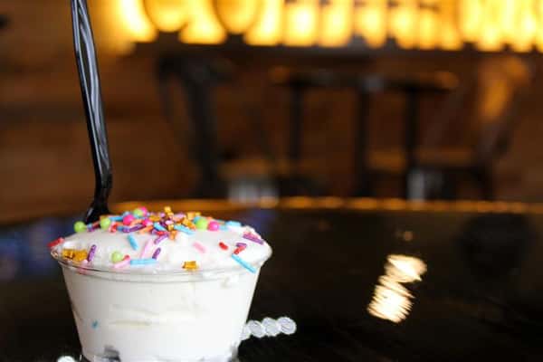 a milkshake with sprinkles on top with the illuminated coffeehouse sign in the background