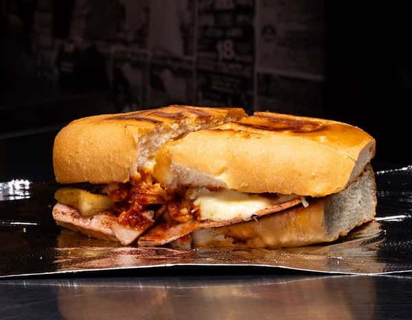 Grilled Mexican torta ahogada stuffed with sliced ham, melted cheese, pineapple, and a rich red salsa on a toasted bolillo roll, served on foil — a savory, saucy sandwich perfect for late-night cravings or authentic taquería menus.