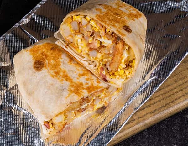 Grilled breakfast burrito stuffed with scrambled eggs, crispy potatoes, bacon, and cheese, cut in half and served on foil-wrapped parchment.