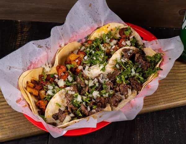 Tray of assorted street-style tacos served on soft corn tortillas, featuring carne asada and al pastor, topped with chopped onions and fresh cilantro — an authentic Mexican dish perfect for taquerías, food trucks, and casual dining menus.