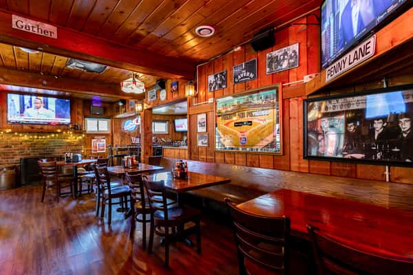 Cozy wood-paneled sports bar with TVs, Beatles memorabilia, string lights, and booth and table seating near a brick fireplace.