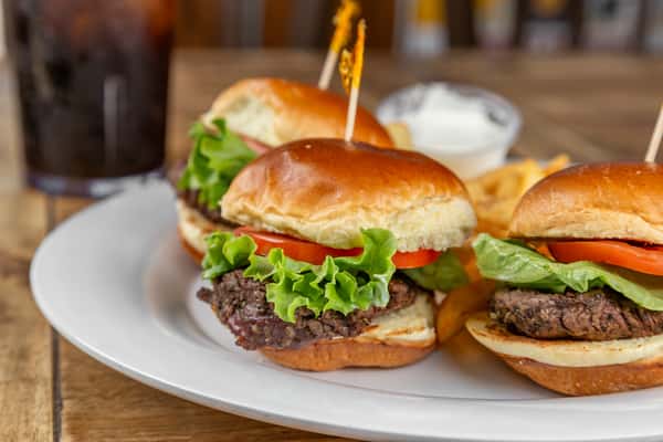 Three beef sliders with lettuce and tomato served with fries and a side of ranch dressing on a white plate.