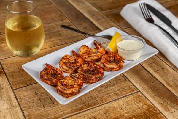Blackened shrimp seasoned with herbs and spices, served with a lemon wedge and side of ranch dressing on a white plate.