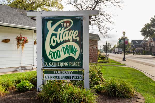 Vintage-style roadside sign for "The Cottage Food/Drink" advertising it as "A Gathering Place" with Tuesday half-price large pizza.