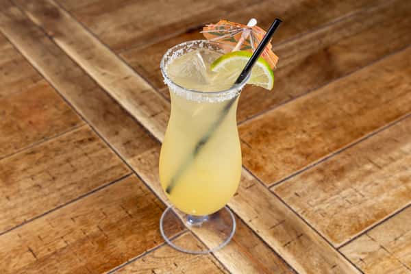 Tropical cocktail with lime slices, ice, and a paper umbrella, served in a salt-rimmed glass with a black straw on a wood table.