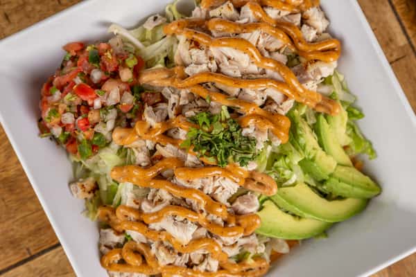 Chopped grilled chicken salad with shredded lettuce, avocado, pico de gallo, and spicy dressing in a white square bowl.