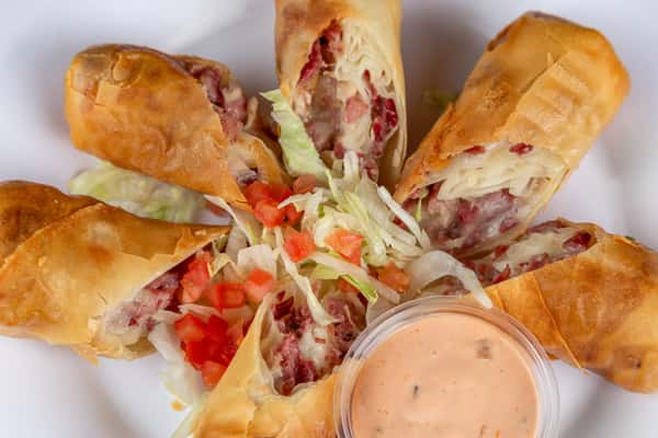 Crispy Reuben egg rolls filled with corned beef and sauerkraut, served with shredded lettuce, diced tomato, and dipping sauce.
