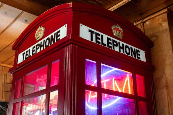 Classic red British-style telephone booth with a glowing neon "OPEN" sign inside, set against a wooden interior wall.