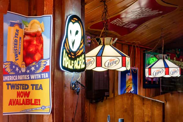 Rustic bar interior with neon signs, Twisted Tea and Miller Lite advertisements, and stained glass-style hanging lights.