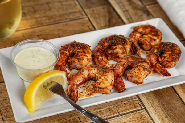 Blackened shrimp seasoned with herbs and spices, served with a lemon wedge and side of ranch dressing on a white plate.
