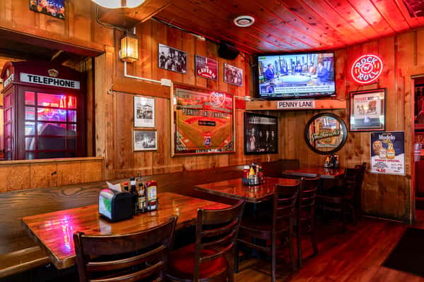 A cozy, wood-paneled dining area featuring a British-style red phone booth, Beatles memorabilia, a neon "Rock 'n' Roll" sign, sports decor, and classic diner-style tables and chairs.