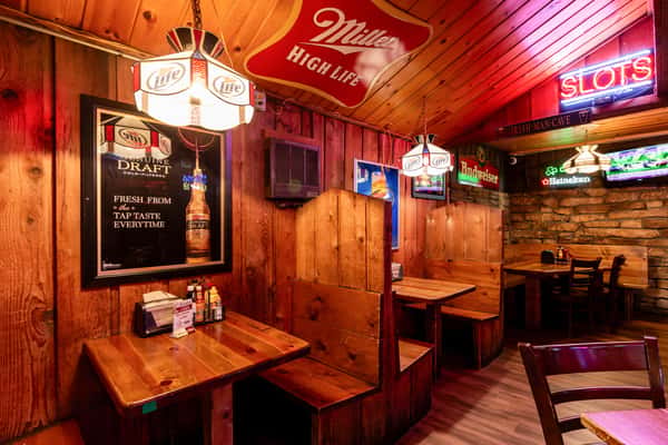 Rustic booth seating area at The Cottage, decorated with vintage beer signs, neon lights, and warm wooden paneling for a cozy pub vibe.