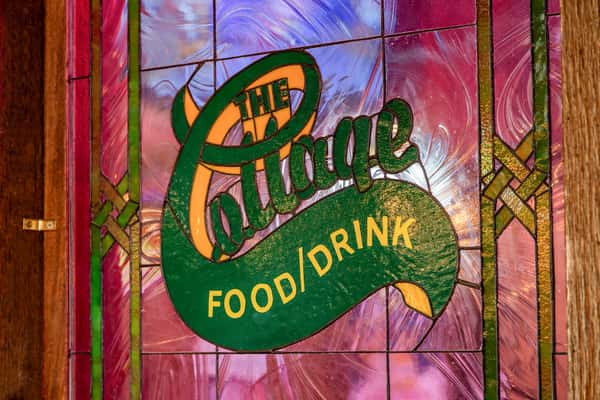 A stained glass panel displaying "The Cottage FOOD/DRINK" with artistic, vintage lettering on a colorful background.