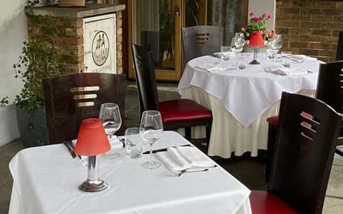Outdoor Don Giovanni dining area with white tablecloths, red lamps, wine glasses, and black chairs with red cushions.