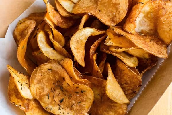 A close-up of a container filled with seasoned, kettle-style potato chips.