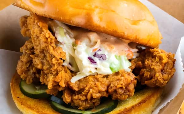 A crispy fried chicken breast on a bun with pickles, coleslaw, and sauce.