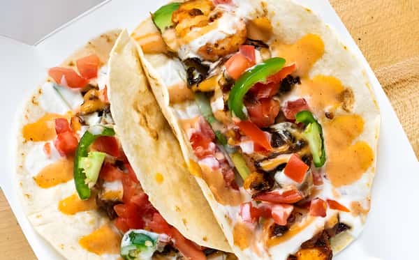 Two flour tacos filled with meat, fresh pico de gallo, green peppers, and a drizzle of sauce.