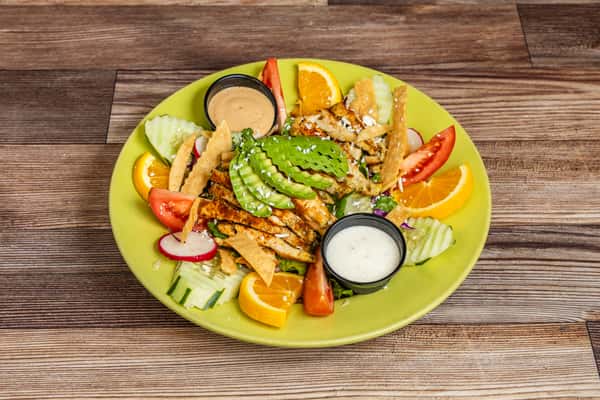 Grilled chicken salad topped with sliced avocado and served with fresh vegetables and dressing