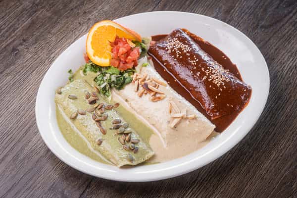 Trio of enchiladas with green, white and mole sauces, garnished with orange