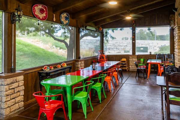 Covered dining area with colorful tables and chairs overlooking the greenery outside