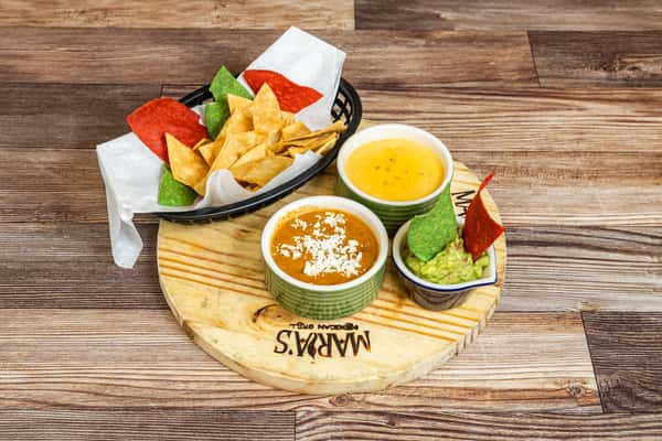 Assorted Mexican dips with guacamole and tortilla chips served on a wooden board